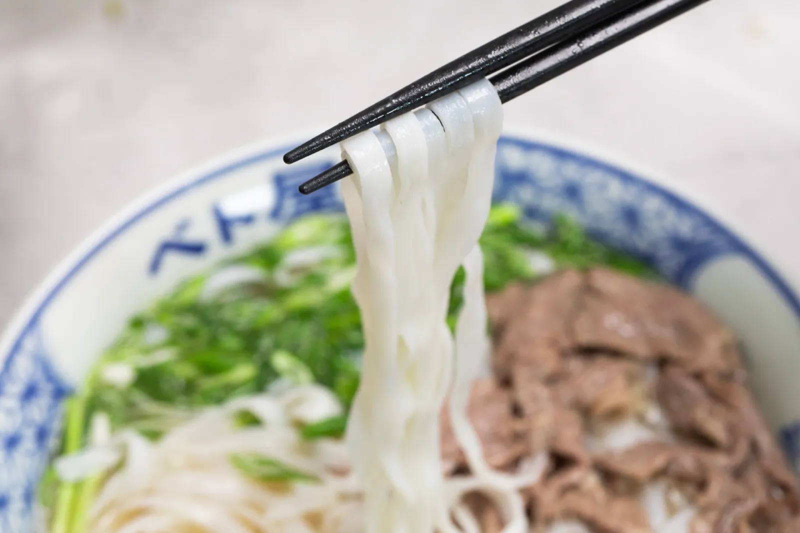 Đũa gắp sợi phở tươi lên khỏi bát phở bò Viet Origin
