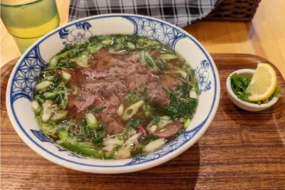 木のトレーにのった、青ねぎとパクチーをたっぷりのせた牛肉のフォーと、レモンとパクチーの小皿、冷たいお茶のグラス