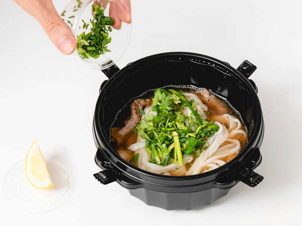 仕上げにパクチーなどの薬味を加える様子。手前にレモン。